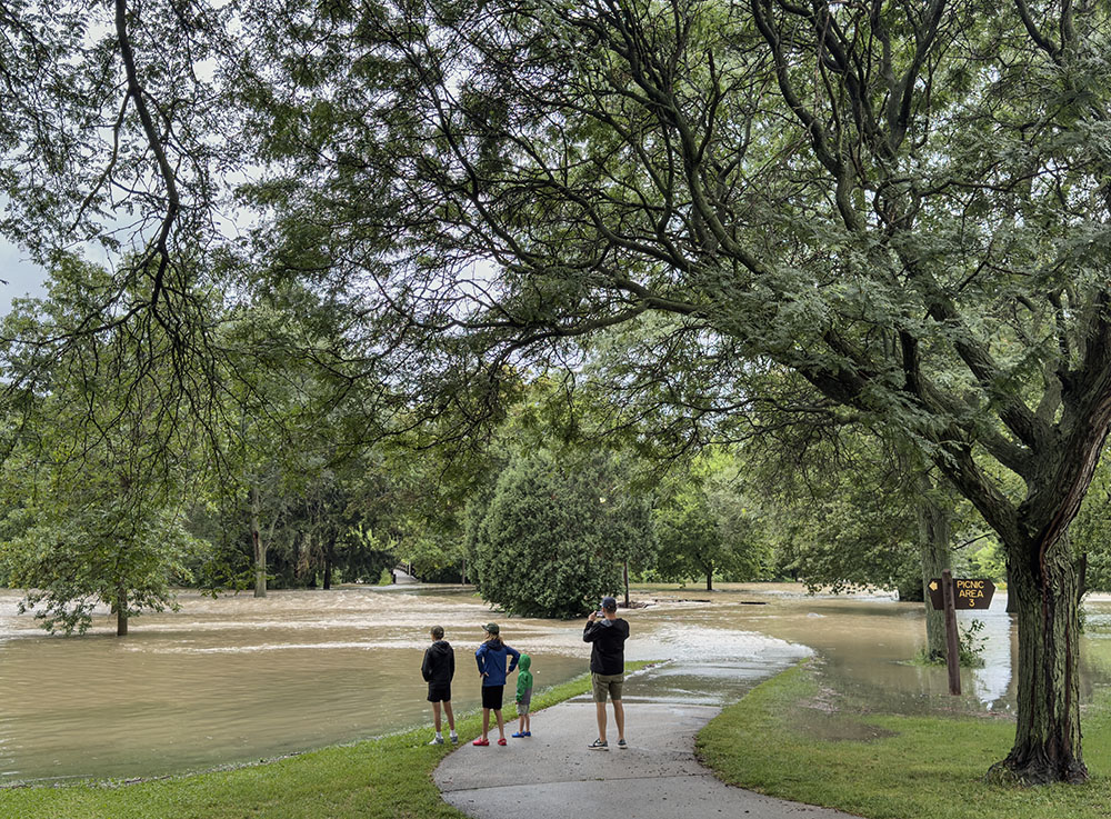 Spectators watch as the Menomonee River flows across Hoyt Park. The actual river is beyond the tree line in the background.