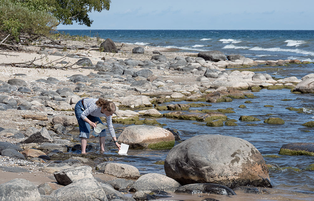 The artist dips her watercolor paper into Lake Michigan to soak it in preparation for sketching.