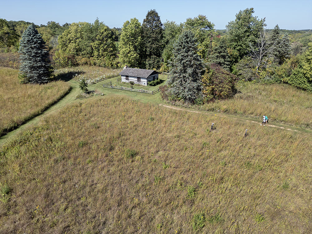 Aerial view of log cabin at the edge of the prairie.