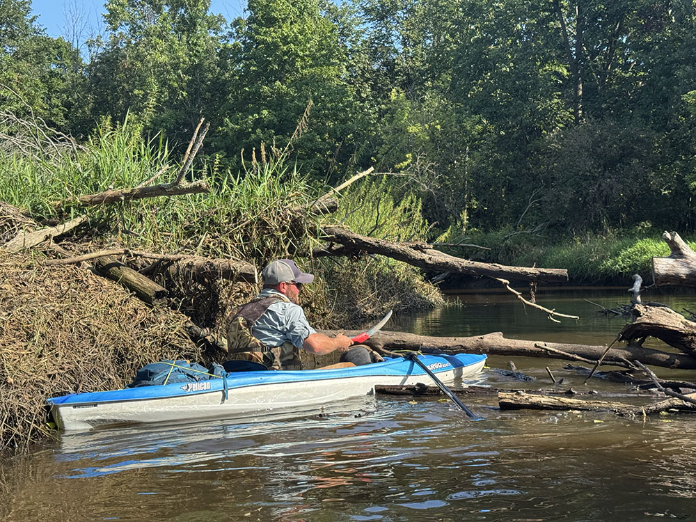Author Steffen Peterson uses a handsaw to remove a small tree fallen across the river.