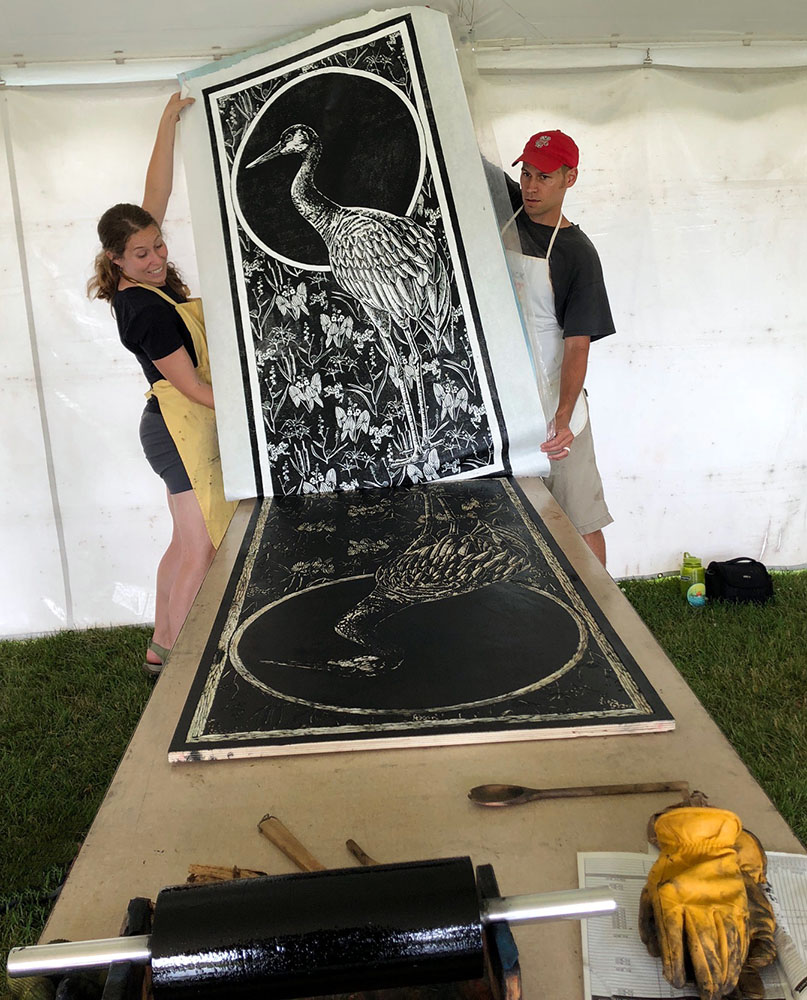 Rebecca Jabs and Anthony Bauer pulling a print of woodcut Marshland Elegy at the 2018 street roller festival Really Big Prints