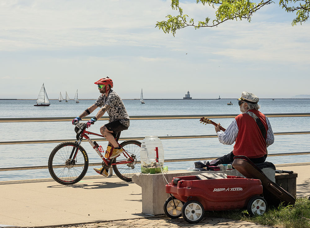 A cyclist passes a busker on the Lakefront promenade.
