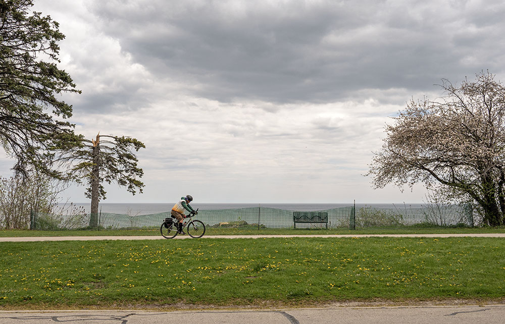 A cyclist on the Oak Leaf Trail pedals past the fenced cliff edge where the bluff collapsed in Sheridan Park.