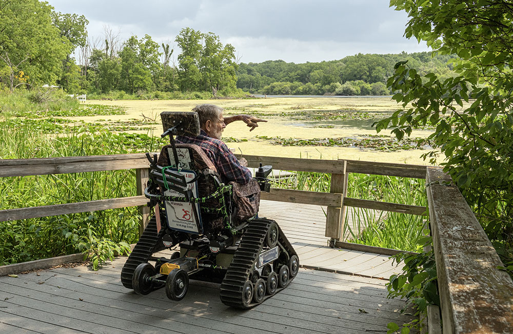 A visitor trying out one of the all-terrain wheelchairs available for visitors pauses for a view of Mallard Lake.