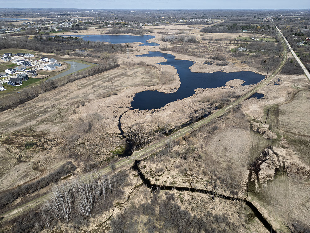 An aerial overview of the Franklin DC property in Franklin. An extension of the Franklin Bike & Hiking Trail is planned to fun along the former rail line, which curves through the middle. This property is contiguous with a unit of the Big Muskego Lake Wildlife Area, background.