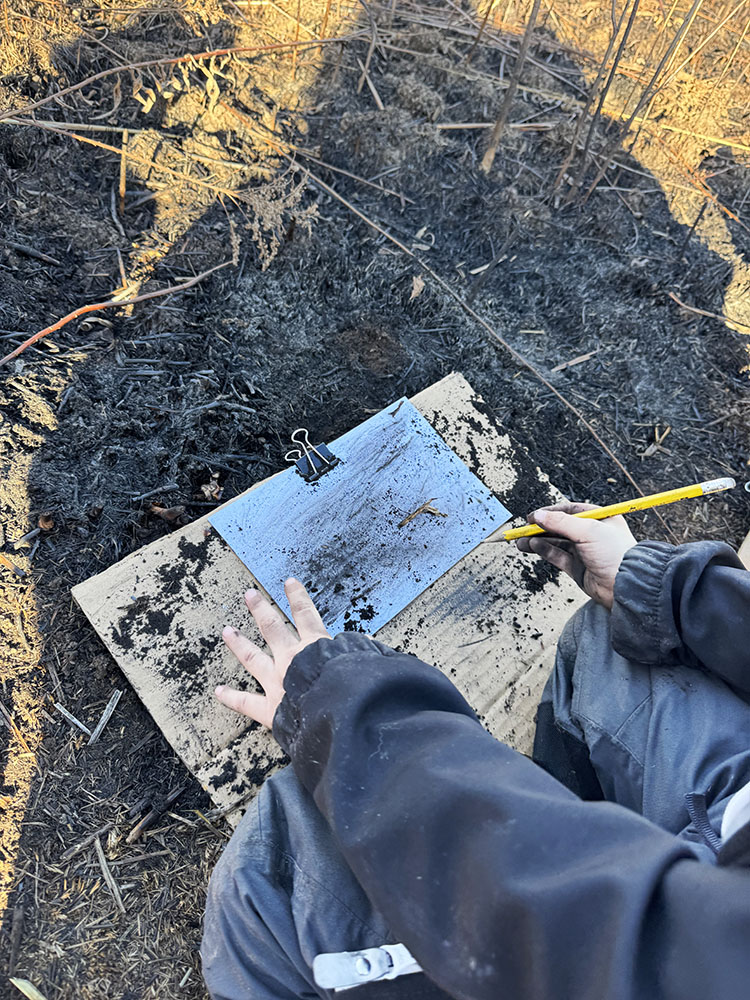 A child explores charcoal and ash from the prairie burn as a medium for art. Photo courtesy Schlitz Audubon Nature Center.