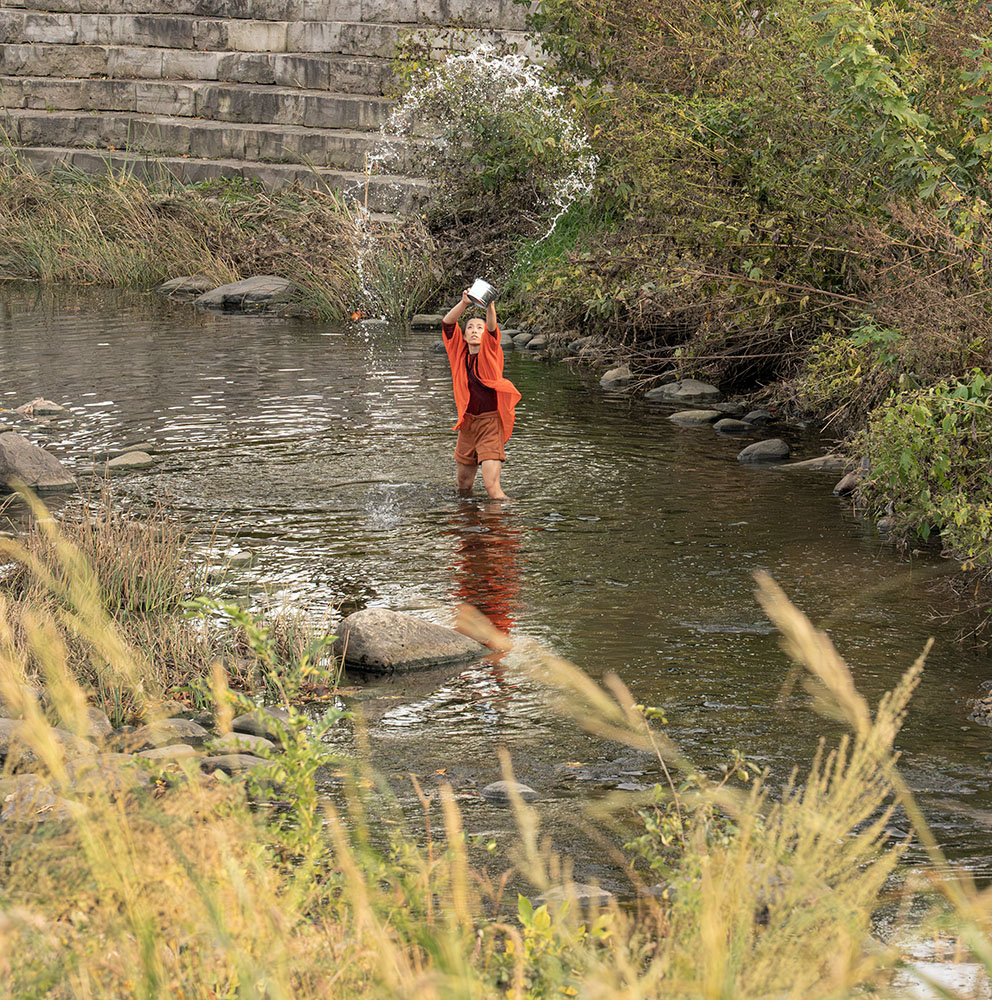 A dancer in the river spraying a bucket of water overhead