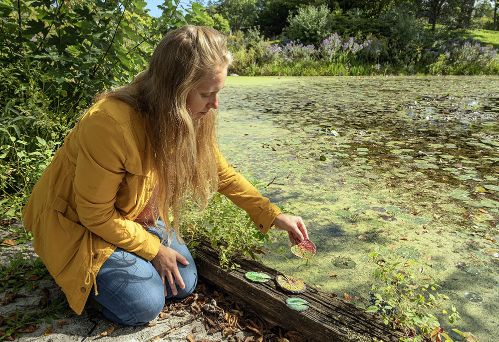 Julie next to the pond with some of her hand-made paper lily pads. Photo by Eddee Daniel